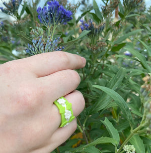 Hand Holding Purple Flower wearing 3 Silicone Rings made of white flower ring and two green leaf rings stacked together
